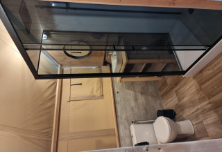 Modern bathroom inside a glamping accommodation featuring a glass shower, toilet, and wood decor.