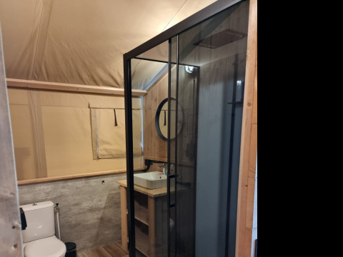 Modernes Badezimmer einer Glamping-Unterkunft mit Glasdusche, Toilette und Holzverkleidung.