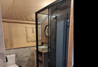 Modern bathroom inside a glamping accommodation featuring a glass shower, toilet, and wood decor.