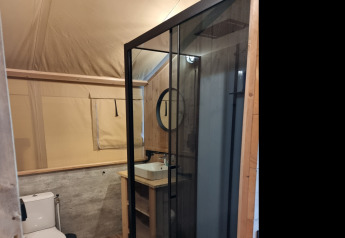 Bagno moderno in una sistemazione glamping con doccia in vetro, wc e decorazioni in legno.
