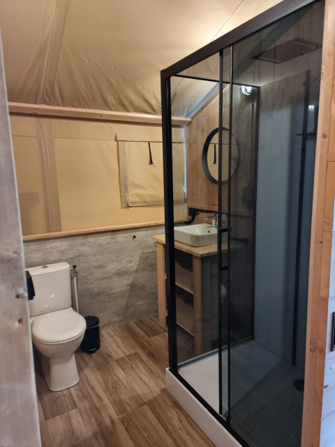 Baño de tienda safari con ducha, inodoro y lavabo en Camping le Roc, Francia, estilo moderno rústico.