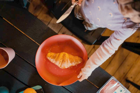 Een kind smeert een croissant op een rood bord in een safaritent op Camping de Haer in Nederland.