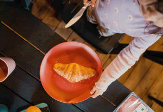 Een kind smeert een croissant op een rood bord in een safaritent op Camping de Haer in Nederland.