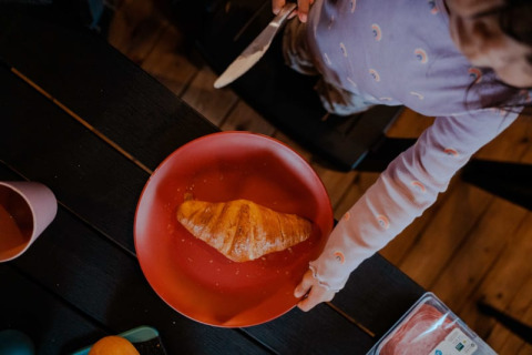 Een kind smeert een croissant op een rood bord in een safaritent op Camping de Haer in Nederland.