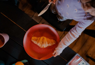 Een kind smeert een croissant op een rood bord in een safaritent op Camping de Haer in Nederland.