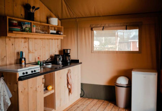 Knusse keuken in een safaritent met houten wanden, keukengerei en raam bij Camping de Haer, Nederland.
