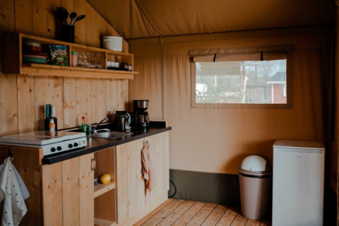 Cozy kitchen setup inside a safari tent with wood paneling, utensils, and a window at Camping de Haer, Netherlands.