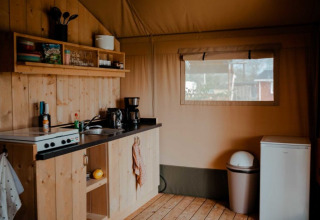 Cozy kitchen setup inside a safari tent with wood paneling, utensils, and a window at Camping de Haer, Netherlands.