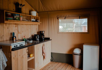 Cozy kitchen setup inside a safari tent with wood paneling, utensils, and a window at Camping de Haer, Netherlands.