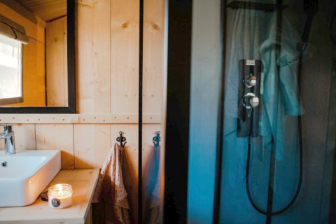 Moderne badkamer in safaritent met wastafel, spiegel, kaarsje en douche bij Camping de Haer, Nederland.