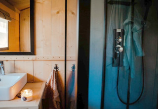 Moderne badkamer in safaritent met wastafel, spiegel, kaarsje en douche bij Camping de Haer, Nederland.