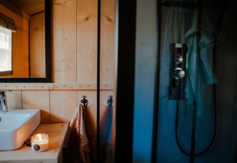 Moderne badeværelse i safaritelt med håndvask, spejl, lys tændt og bruser ved Camping de Haer, Holland.