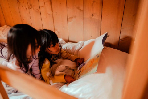 Twee kinderen lezen samen een boek op een gezellig bed in een safaritent bij Camping de Haer, Nederland.