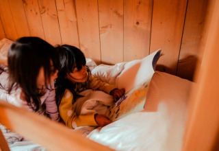 Twee kinderen lezen samen een boek op een gezellig bed in een safaritent bij Camping de Haer, Nederland.