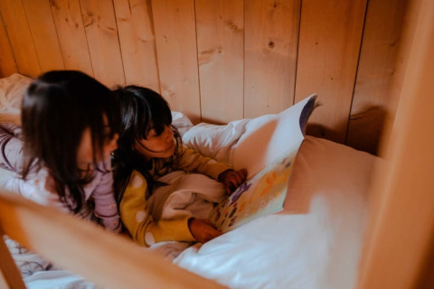 Due bambini leggono un libro insieme su un letto accogliente in una tenda safari al Camping de Haer, Paesi Bassi.