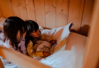 Two children reading a book together on a cozy bed inside a safari tent at Camping de Haer, Netherlands.