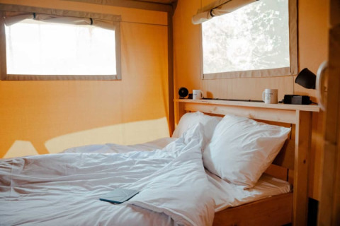 Interior of Safari tent + sanitary, featuring a cozy bed with white bedding, windows, and wooden shelves.