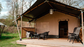 Safaritent met sanitair op houten terras, zithoek buiten in een groene, natuurlijke omgeving