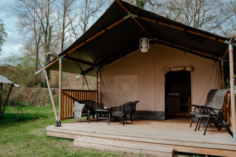 Safari tent with private bathroom on wooden deck, outdoor seating area set in a lush, green landscape