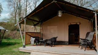 Safari tent with private bathroom on wooden deck, outdoor seating area set in a lush, green landscape