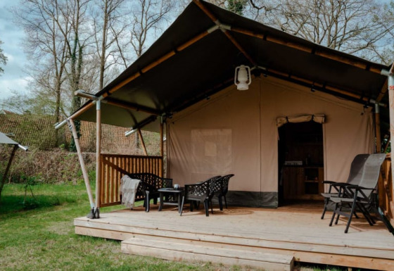 Safari tent with private bathroom on wooden deck, outdoor seating area set in a lush, green landscape