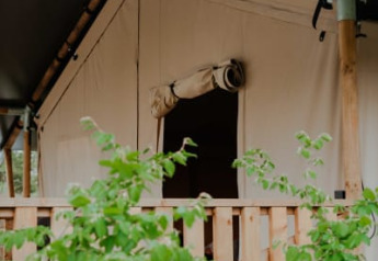 Safaritent met houten veranda en eigen sanitair bij Camping de Haer in Nederland, omgeven door groen.