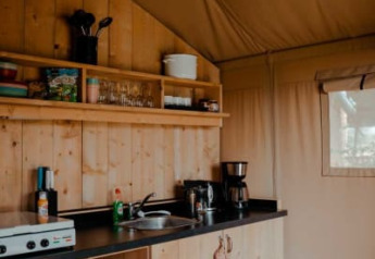Cozy kitchenette with wooden cabinets and camping essentials inside a safari tent at Camping de Haer, Netherlands.