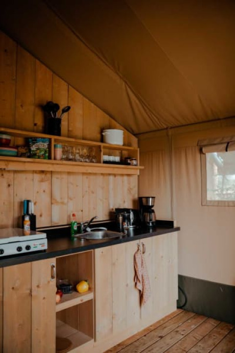 Pequeña cocina acogedora con armarios de madera en tienda safari en Camping de Haer, Países Bajos.