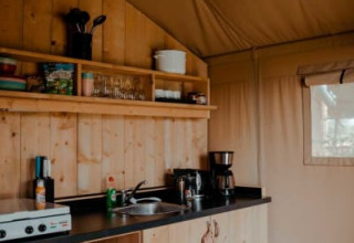 Cozy kitchenette with wooden cabinets and camping essentials inside a safari tent at Camping de Haer, Netherlands.