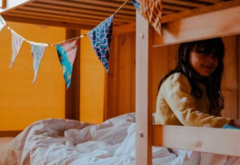 A child sits on the lower bunk bed inside a safari tent with bunting at Camping de Haer, Netherlands.