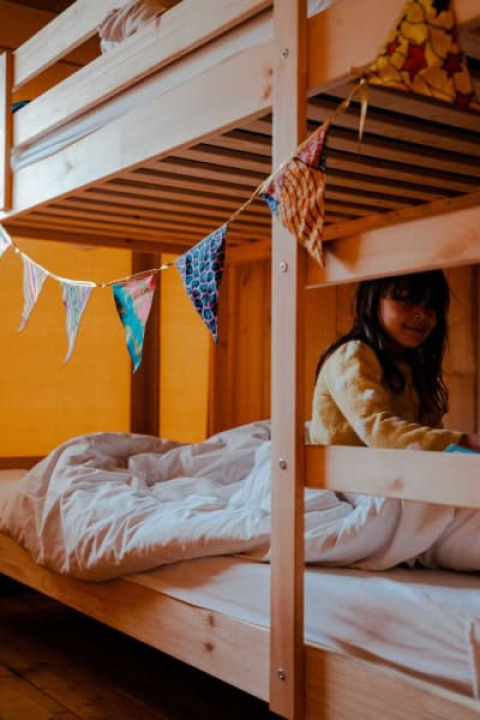 A child sits on the lower bunk bed inside a safari tent with bunting at Camping de Haer, Netherlands.