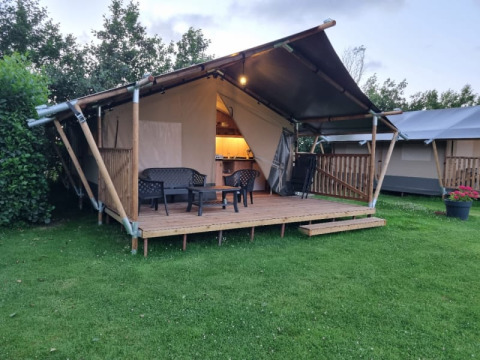 Safari-Zelt mit Sanitäranlagen, Holzterrasse und Sitzbereich im Grünen auf einem gepflegten Rasen.