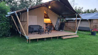 Tienda safari con baño, terraza de madera y zona de estar al aire libre sobre césped verde.