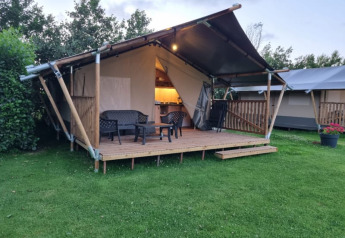 Tienda safari con baño, terraza de madera y zona de estar al aire libre sobre césped verde.