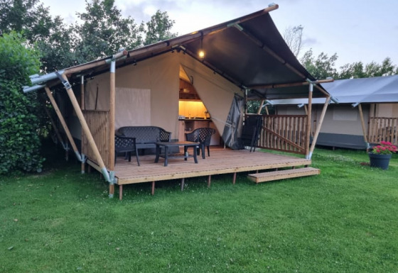 Tienda safari con baño, terraza de madera y zona de estar al aire libre sobre césped verde.