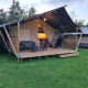Safari telt med sanitære faciliteter, træterrasse og udendørs siddepladser på grøn græsplæne.