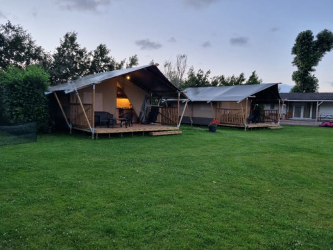 Two safari tents with private decks at Camping de Tulpenweide in the Netherlands, set on a green lawn.