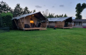 To safaritelt med veranda på Camping de Tulpenweide i Holland, omgivet af grønt græs og træer.