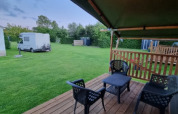 Safari tent with covered patio, outdoor seating, and view of caravan and grass at Camping de Tulpenweide.