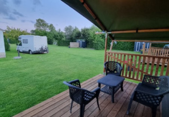 Tienda safari con terraza cubierta, asientos exteriores y vista de una caravana en Camping de Tulpenweide.