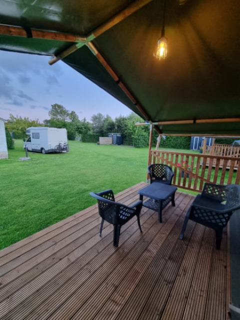 Tenda safari con patio coperto, sedie e vista su caravan e prato al Camping de Tulpenweide nei Paesi Bassi.