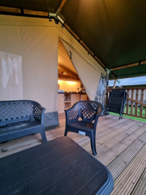 Safari tent with deck and plastic chairs at Camping de Tulpenweide in the Netherlands, kitchen inside.