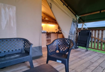 Safari tent with deck and plastic chairs at Camping de Tulpenweide in the Netherlands, kitchen inside.