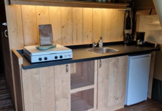 Kitchen space in a safari tent at Camping de Tulpenweide, Netherlands, featuring wood cupboards, stove, and fridge.