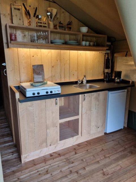 Kitchen space in a safari tent at Camping de Tulpenweide, Netherlands, featuring wood cupboards, stove, and fridge.