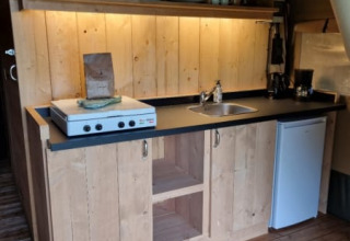 Keukenruimte in safaritent op Camping de Tulpenweide, Nederland, met houten kasten, fornuis en kleine koelkast.