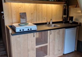 Kitchen space in a safari tent at Camping de Tulpenweide, Netherlands, featuring wood cupboards, stove, and fridge.