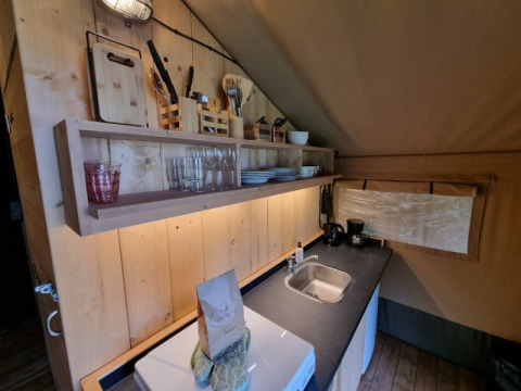 Küchenbereich im Safarizelt mit Holzregalen, Geschirr, Besteck und Spüle auf Camping de Tulpenweide.