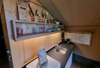 Cucina in tenda safari con scaffali di legno, stoviglie e lavandino al Camping de Tulpenweide, Paesi Bassi.