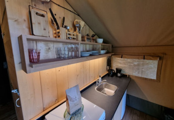 Cuisine sous tente safari avec étagères en bois, vaisselle, ustensiles et évier au Camping de Tulpenweide.